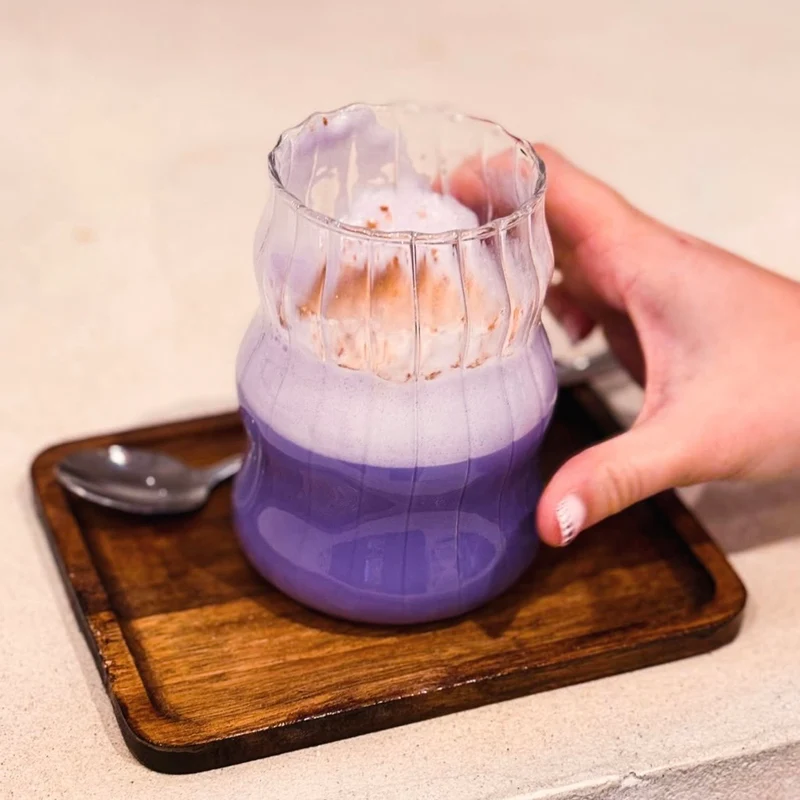 Ube Latte van Ube Nolia in een geribbeld glas op een houten dienblad